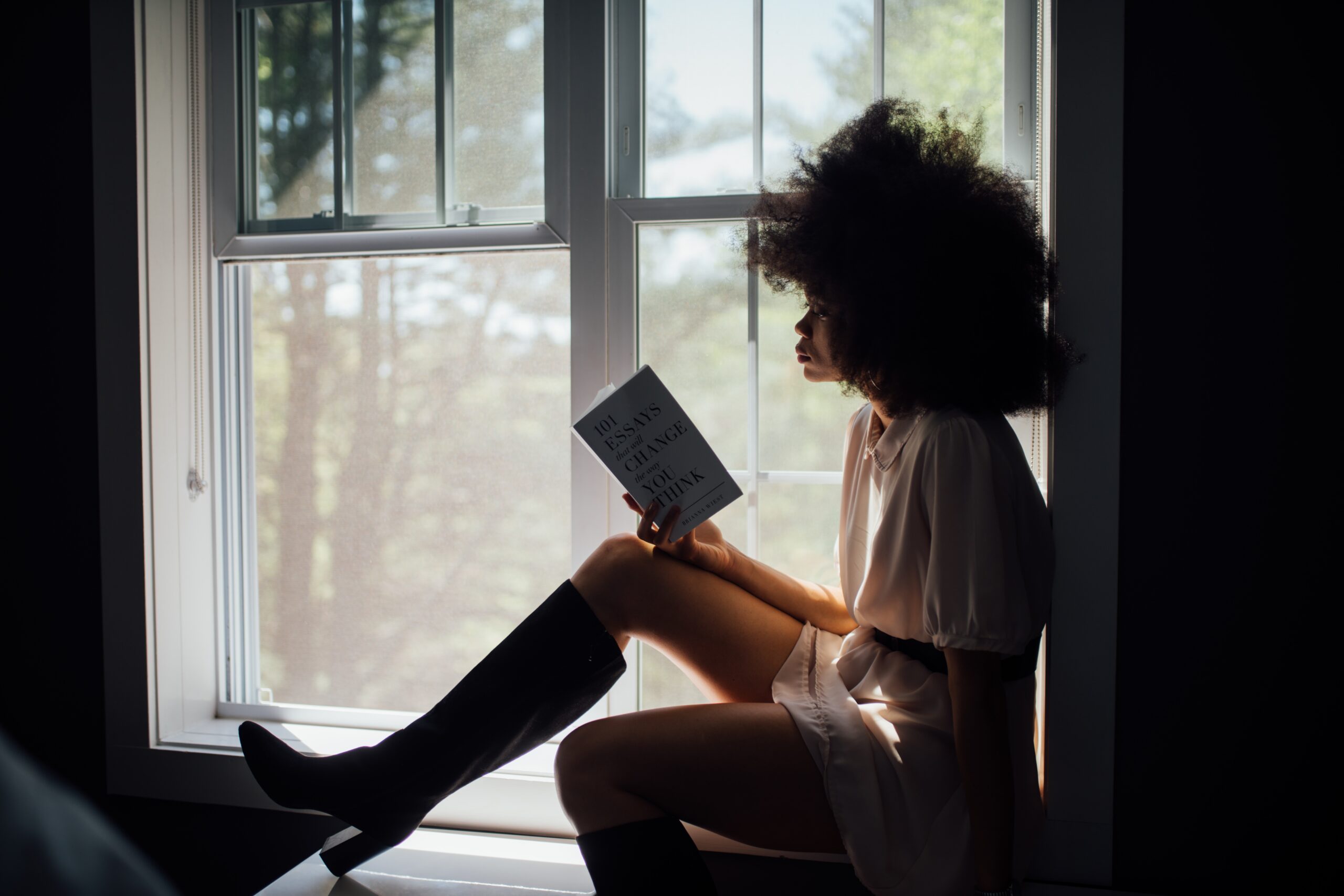 a woman sits in a window sill and reads a book